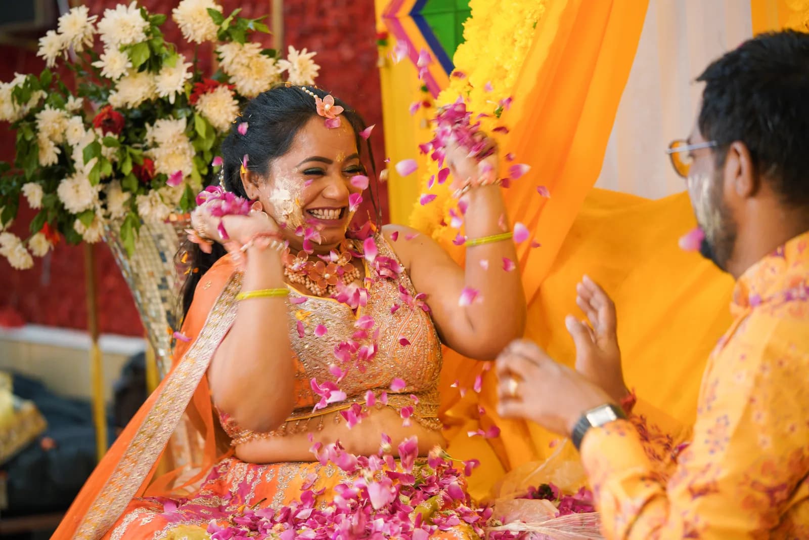 Groom laughing with guests at reception table, photographer out of focus in background, natural lighting